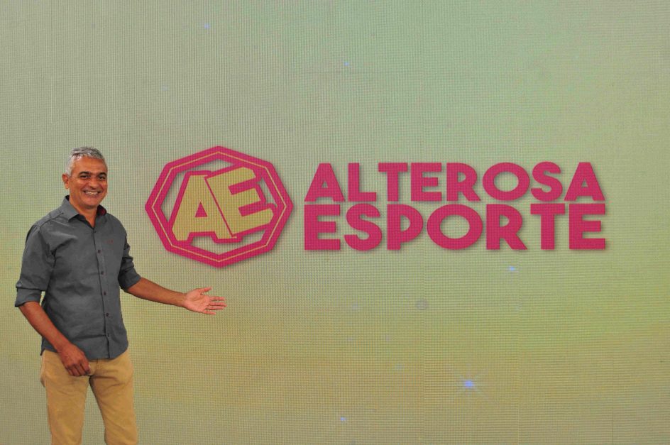 Leopoldo Siqueira, apresentador do Alterosa Esporte, posa em frente a um telão de led que exibe a marca do programa